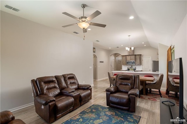 living area with visible vents, light wood finished floors, baseboards, arched walkways, and ceiling fan with notable chandelier