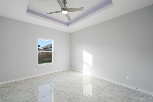 empty room featuring a raised ceiling, baseboards, marble finish floor, and ceiling fan