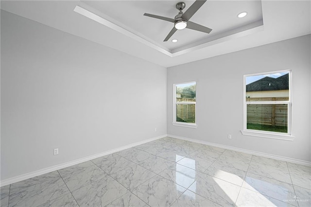spare room with marble finish floor, a raised ceiling, and baseboards