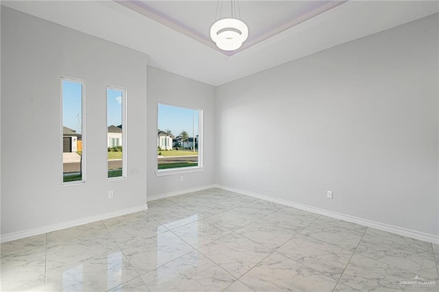 empty room with a tray ceiling, baseboards, and marble finish floor