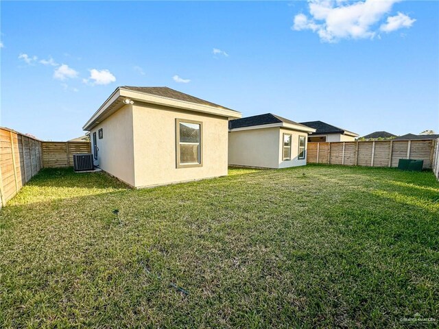 rear view of house with central AC unit, a lawn, a fenced backyard, and stucco siding