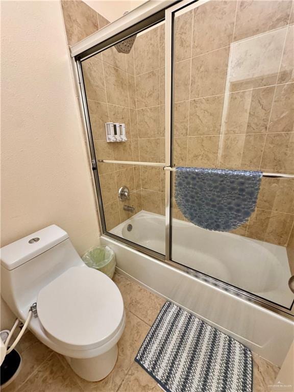 bathroom with tile patterned floors, bath / shower combo with glass door, and toilet