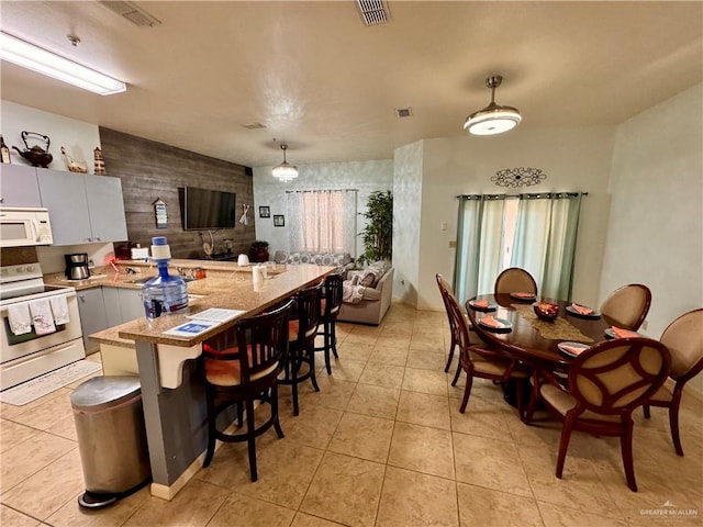 kitchen with kitchen peninsula, a breakfast bar, white appliances, pendant lighting, and light tile patterned flooring