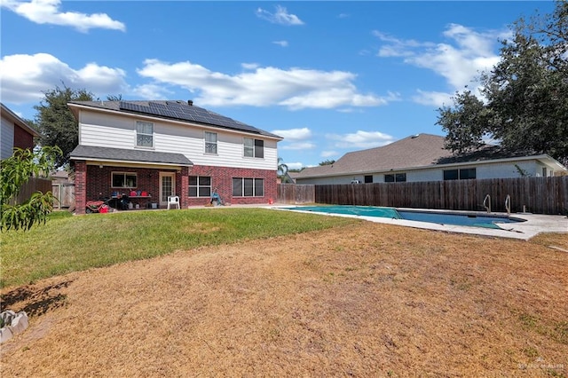 rear view of house with a yard, a patio, solar panels, and a covered pool