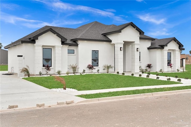 view of front facade featuring stucco siding, roof with shingles, and a front yard