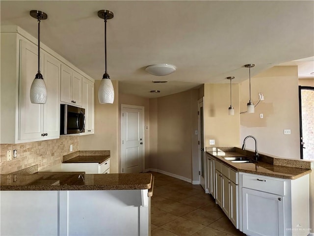 1311 Anahi St, Alamo, TX 78516 - kitchen featuring stainless steel microwave, a peninsula, a sink, white cabinets, and decorative backsplash