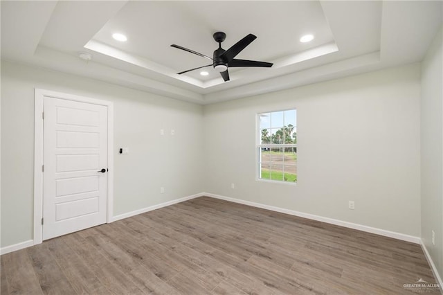 empty room featuring hardwood / wood-style flooring, ceiling fan, and a tray ceiling