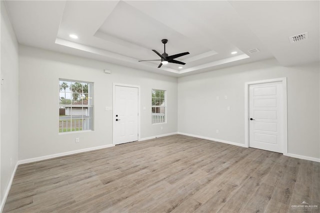 empty room featuring a tray ceiling, ceiling fan, and light hardwood / wood-style flooring