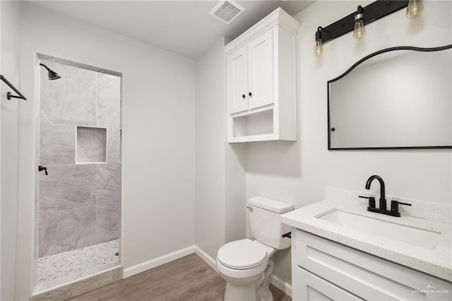 bathroom with a tile shower, vanity, wood-type flooring, and toilet