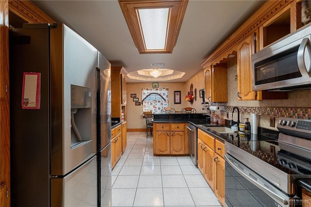 kitchen with kitchen peninsula, appliances with stainless steel finishes, sink, light tile patterned floors, and dark stone countertops