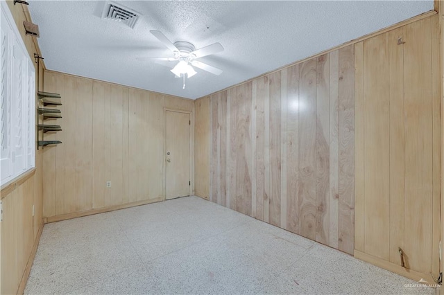 unfurnished room featuring wood walls, ceiling fan, and a textured ceiling