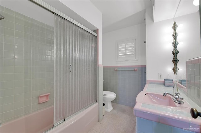 full bathroom featuring vanity, bath / shower combo with glass door, tile walls, and toilet