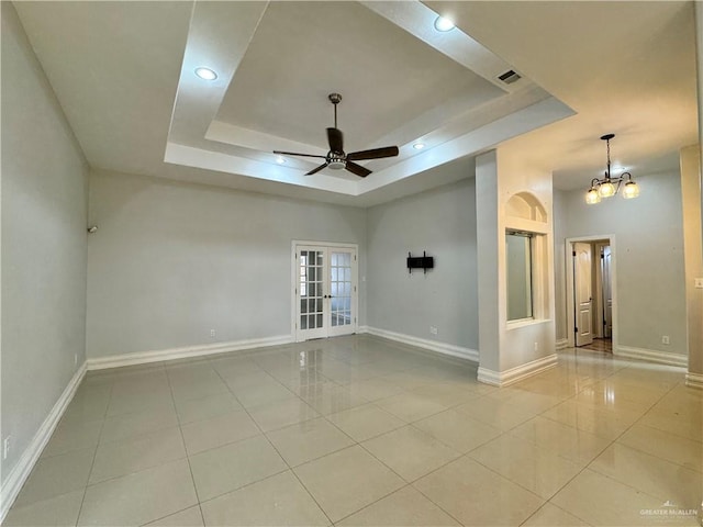 tiled empty room featuring ceiling fan with notable chandelier, french doors, and a tray ceiling