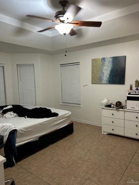 bedroom with ceiling fan, a tray ceiling, and light tile patterned floors