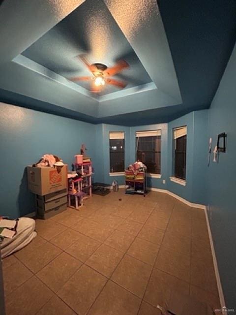 game room featuring ceiling fan, tile patterned floors, a tray ceiling, and a textured ceiling