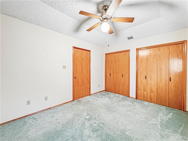 unfurnished bedroom featuring carpet, ceiling fan, a textured ceiling, and multiple closets