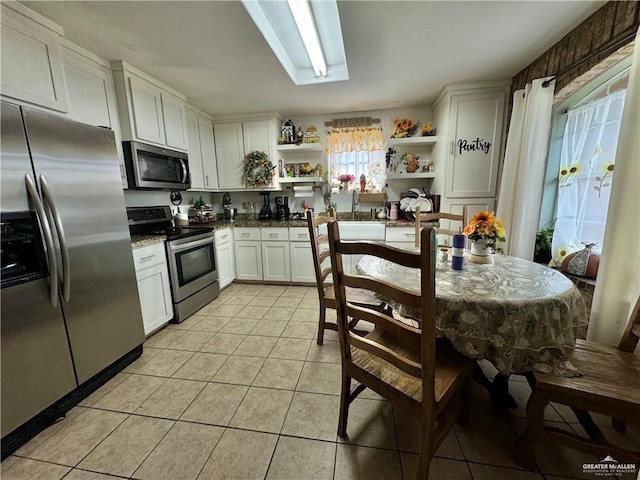 kitchen featuring a skylight, white cabinets, stainless steel appliances, and light tile patterned floors