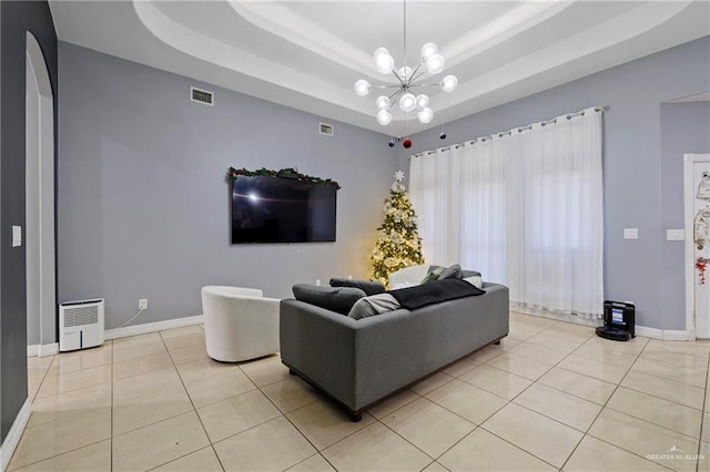 living room with light tile patterned flooring, an inviting chandelier, and a tray ceiling