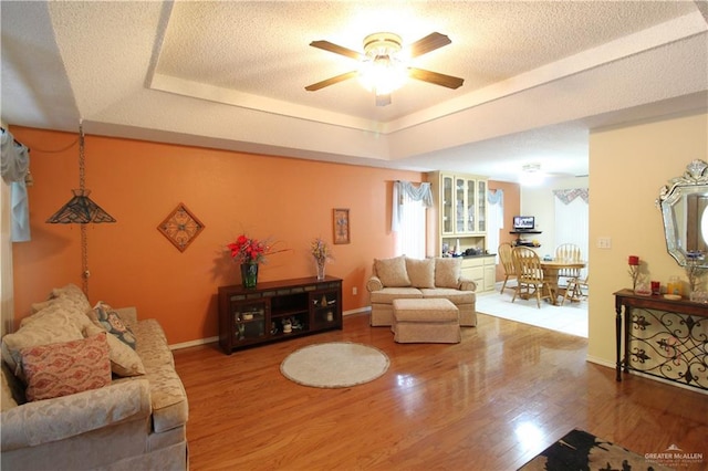 living room featuring ceiling fan, a tray ceiling, hardwood / wood-style floors, and a textured ceiling