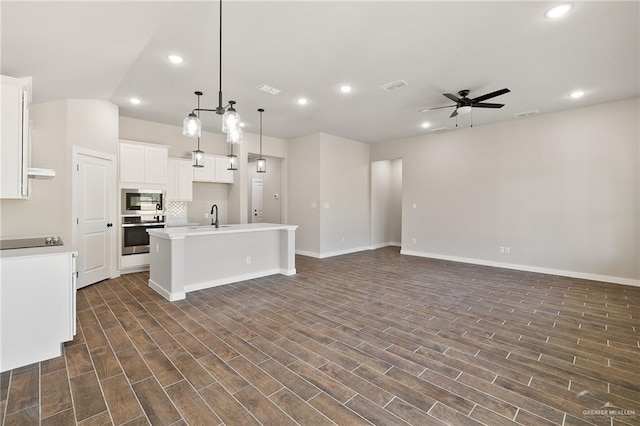 kitchen featuring built in microwave, white cabinetry, stainless steel oven, a center island with sink, and pendant lighting