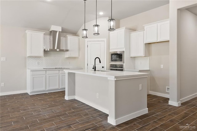 kitchen with appliances with stainless steel finishes, an island with sink, sink, white cabinets, and wall chimney range hood