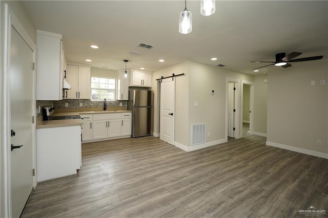 kitchen featuring white cabinetry, sink, a barn door, stainless steel fridge, and decorative light fixtures