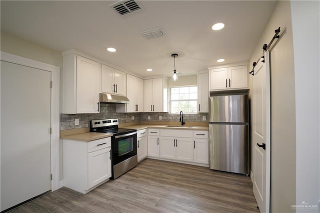 kitchen with white cabinetry, sink, stainless steel appliances, a barn door, and pendant lighting