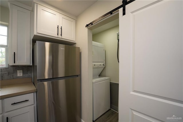 clothes washing area featuring a barn door, stacked washing maching and dryer, and dark hardwood / wood-style floors