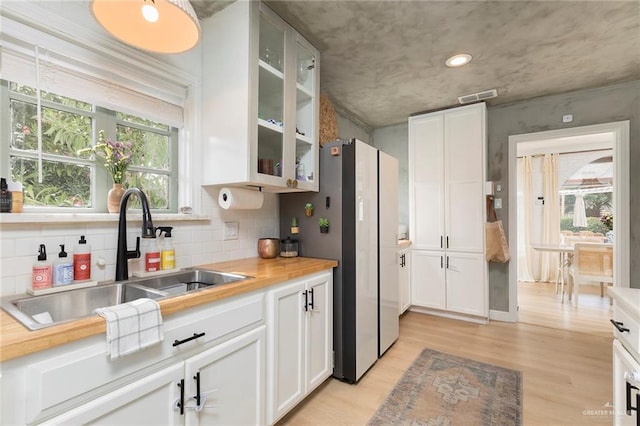 1011 W Orange St, Mcallen, TX 78501 - kitchen with light wood-type flooring, white cabinets, glass insert cabinets, backsplash, and freestanding refrigerator