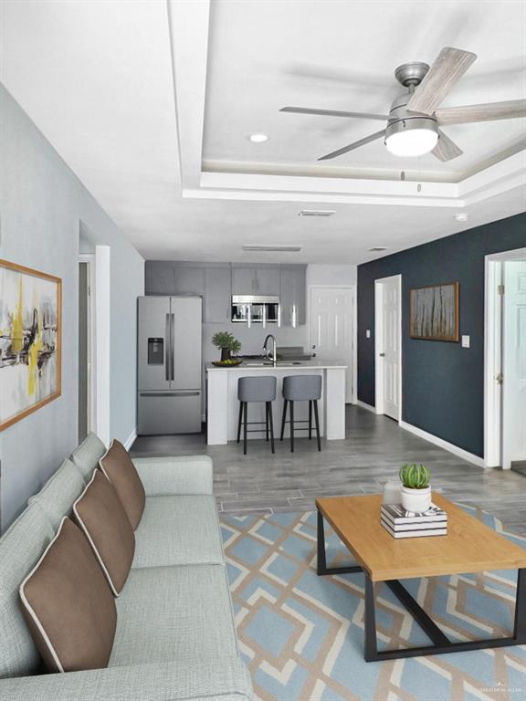 living room with a raised ceiling, ceiling fan, dark hardwood / wood-style flooring, and sink