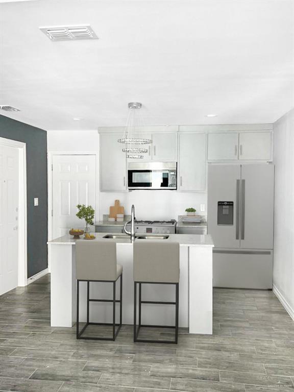 kitchen featuring wood-type flooring, stainless steel appliances, white cabinetry, and a kitchen island with sink