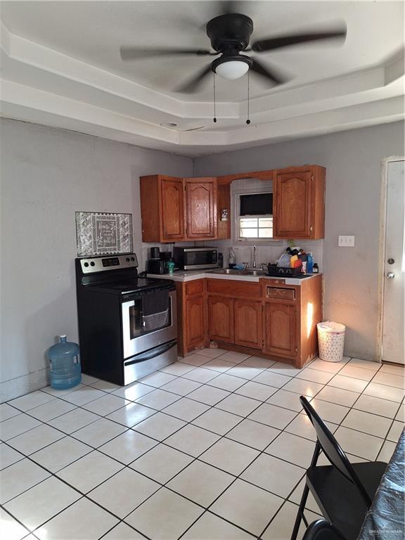 kitchen featuring sink, ceiling fan, light tile patterned floors, appliances with stainless steel finishes, and a tray ceiling