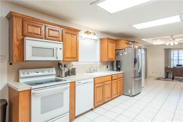 kitchen with ceiling fan, sink, a tray ceiling, white appliances, and light tile patterned floors