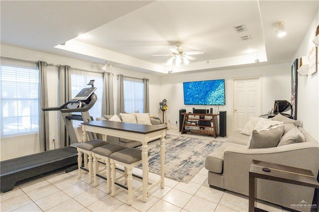 living room featuring a raised ceiling, light tile patterned floors, and ceiling fan