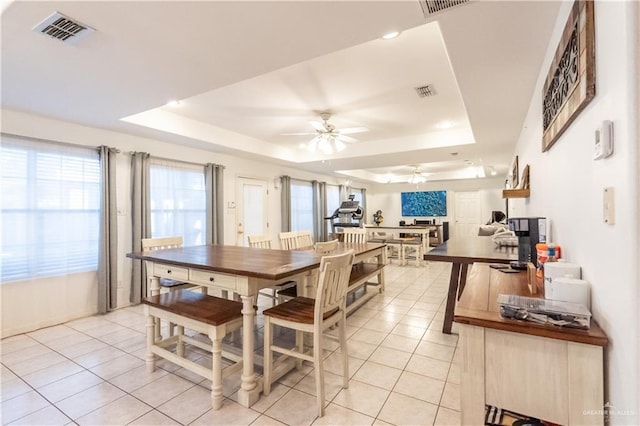 tiled dining area with ceiling fan and a tray ceiling