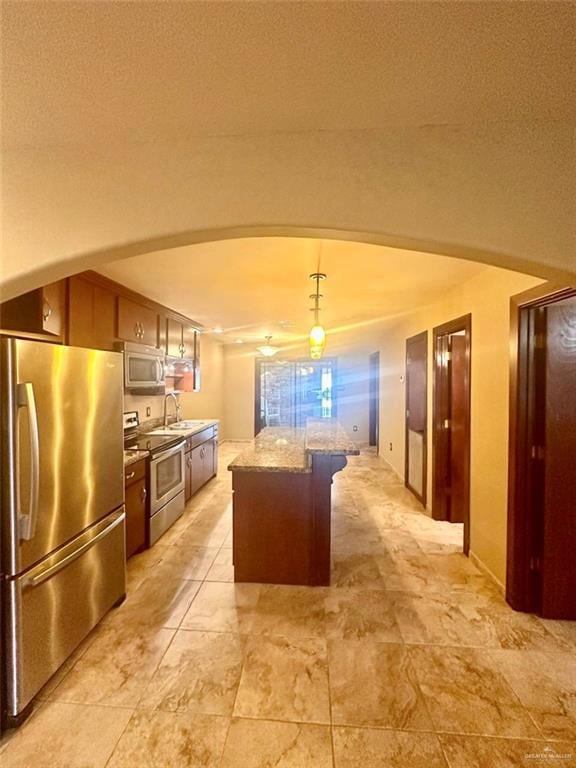 kitchen featuring light stone countertops, appliances with stainless steel finishes, a textured ceiling, a center island, and hanging light fixtures