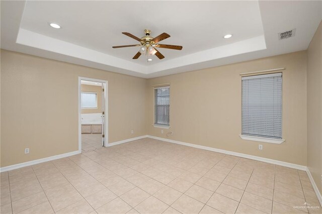 empty room with ceiling fan, light tile patterned floors, and a tray ceiling