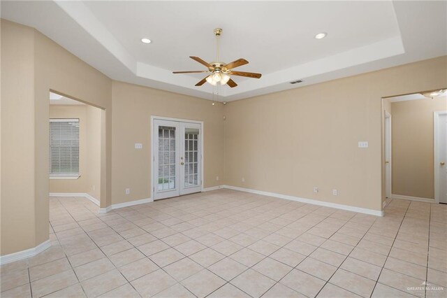 unfurnished room featuring a tray ceiling, ceiling fan, french doors, and light tile patterned flooring