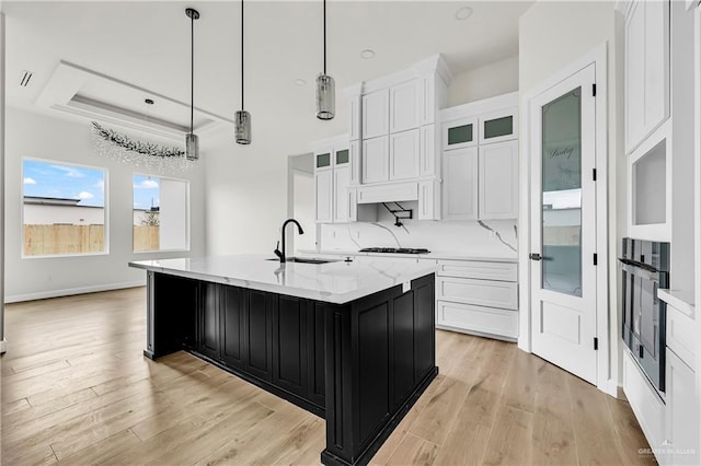 kitchen featuring sink, wall oven, an island with sink, white cabinets, and decorative light fixtures