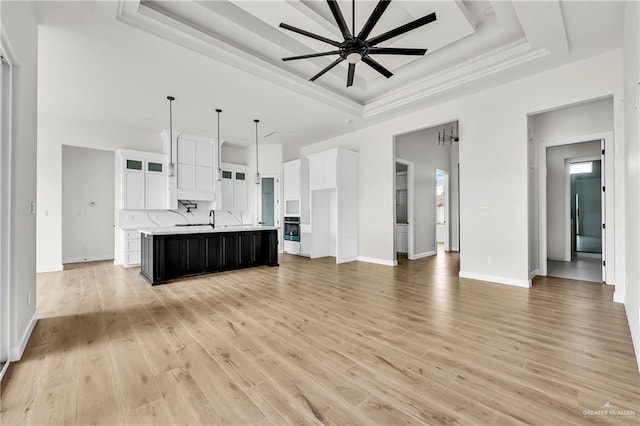 kitchen featuring white cabinetry, a tray ceiling, an island with sink, and hanging light fixtures