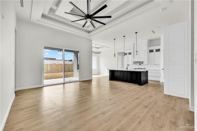 kitchen featuring white cabinetry, hanging light fixtures, a kitchen island with sink, light hardwood / wood-style floors, and a tray ceiling