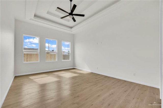 empty room with ceiling fan, a tray ceiling, and light hardwood / wood-style floors