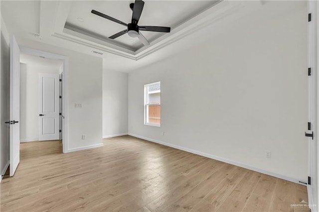 spare room featuring a raised ceiling, ceiling fan, and light hardwood / wood-style floors