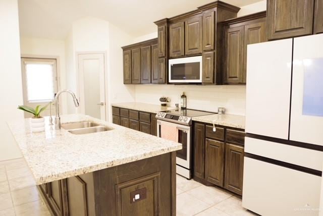 kitchen with a center island with sink, sink, electric range, white fridge, and dark brown cabinetry