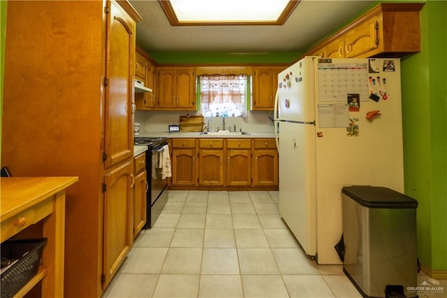 kitchen with light tile patterned floors, white fridge, black range oven, and sink