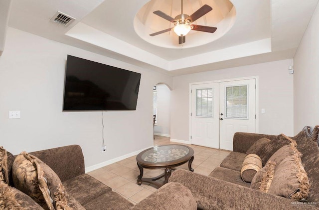 living room with ceiling fan, arched walkways, a tray ceiling, and visible vents