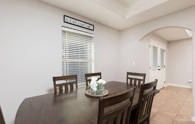 dining area featuring arched walkways, baseboards, and light tile patterned floors