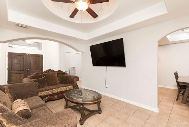 living area with arched walkways, a raised ceiling, visible vents, and a ceiling fan