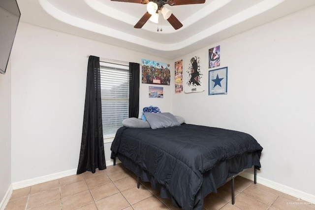 bedroom featuring light tile patterned flooring, a raised ceiling, a ceiling fan, and baseboards