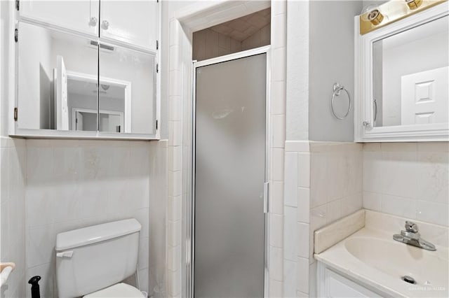 bathroom featuring vanity, toilet, a shower with door, and tile walls